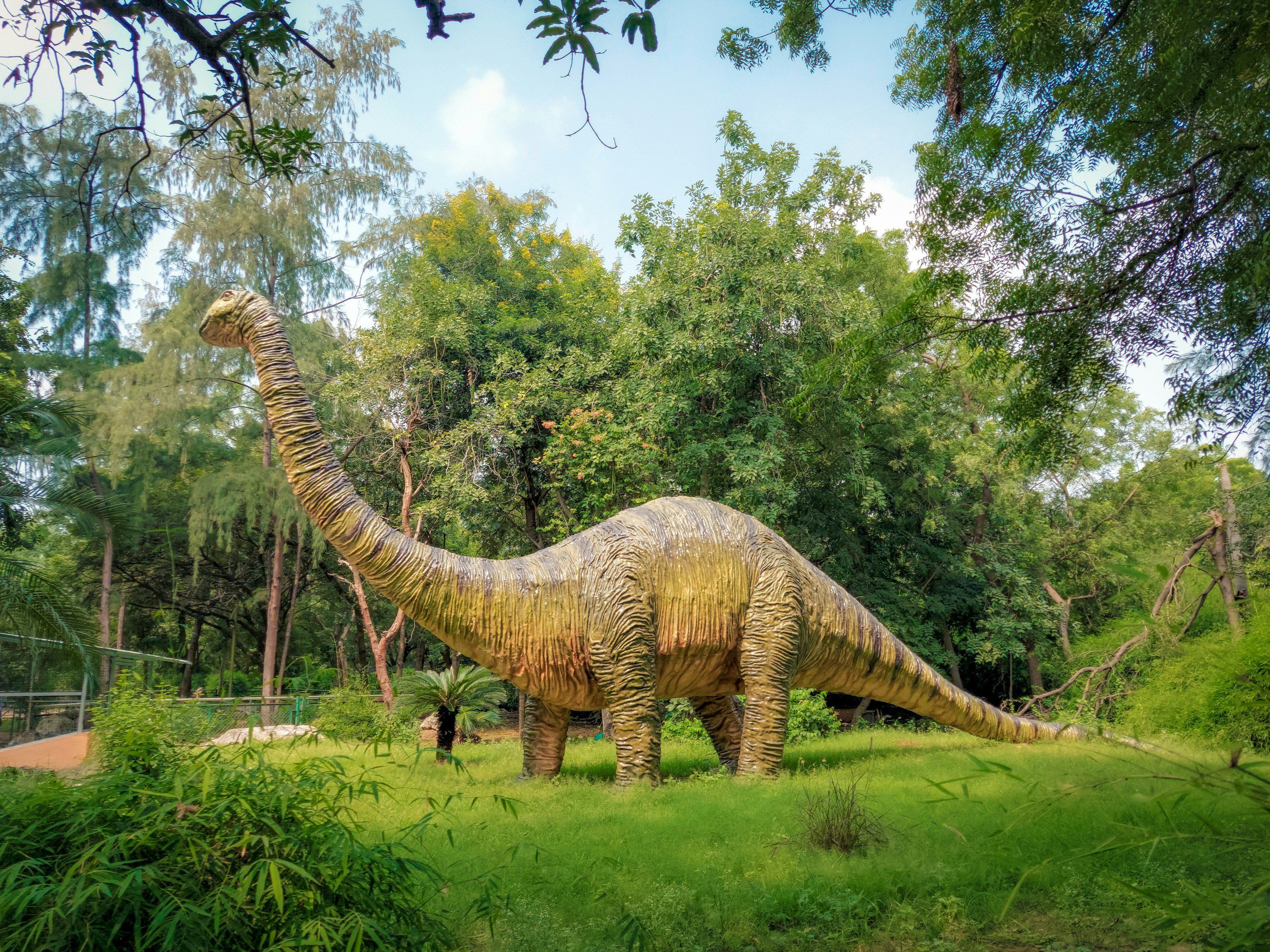 A large dinosaur statue stands amidst lush greenery in a wooded area.