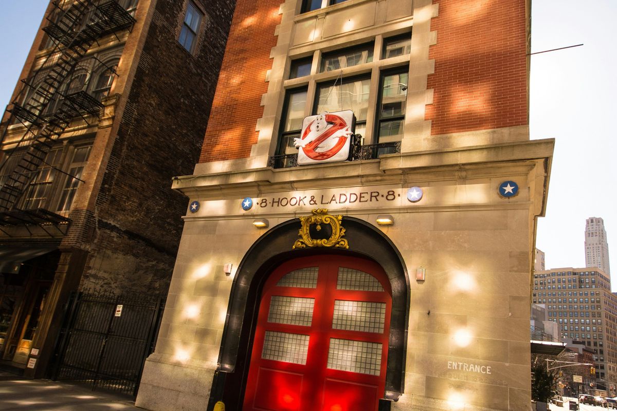 Firehouse with red doors and Ghostbusters logo, sunlight on brick facade.