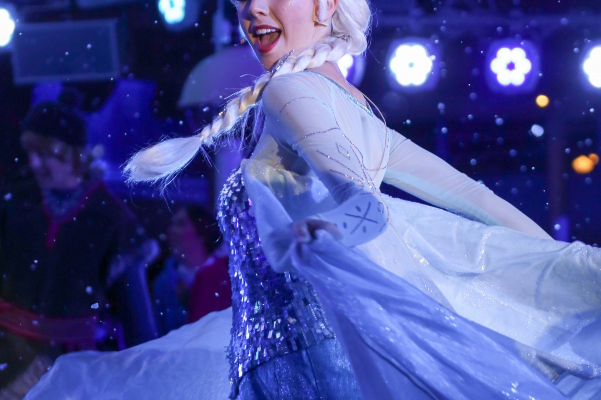 Elsa in a sparkly blue costume and white wig, dancing in falling snow.