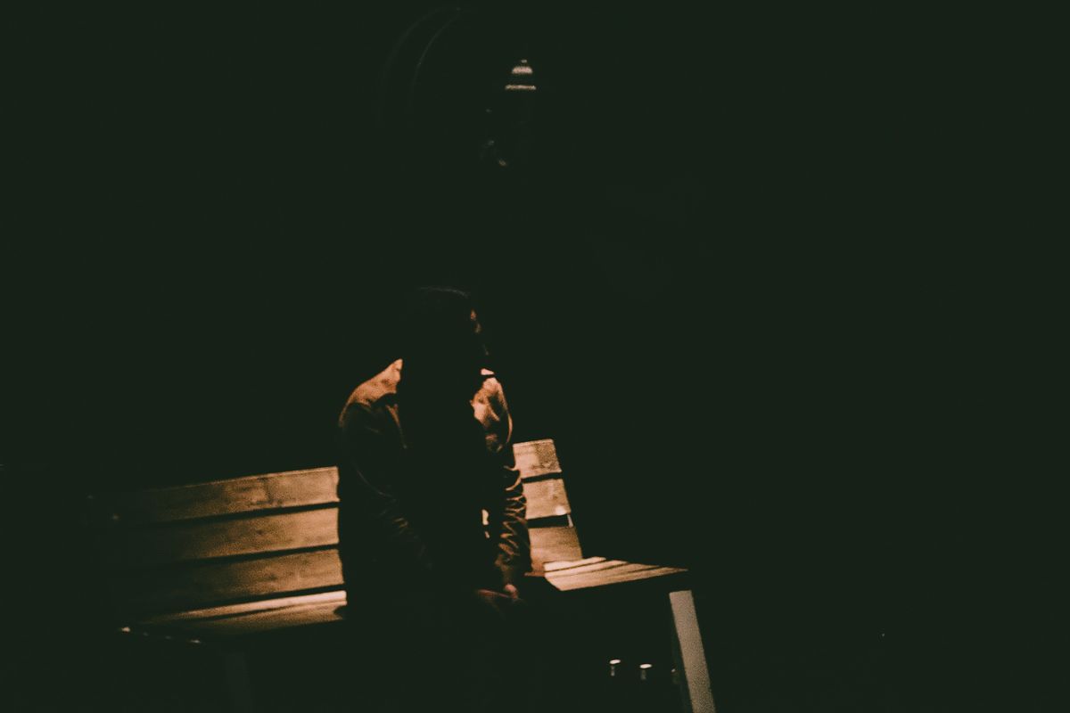 Person sitting alone on a dimly lit bench in the dark.