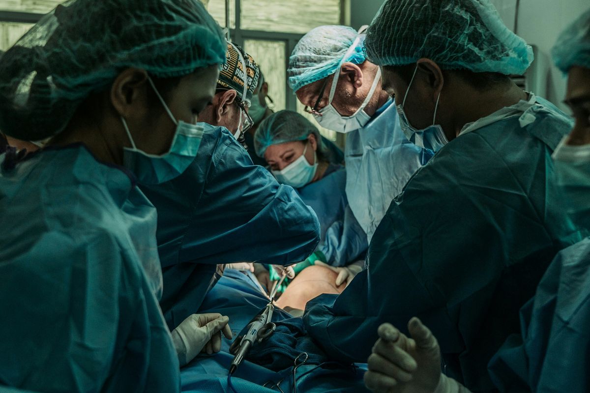 Surgical team operating in a hospital under bright light, wearing green scrubs and masks.