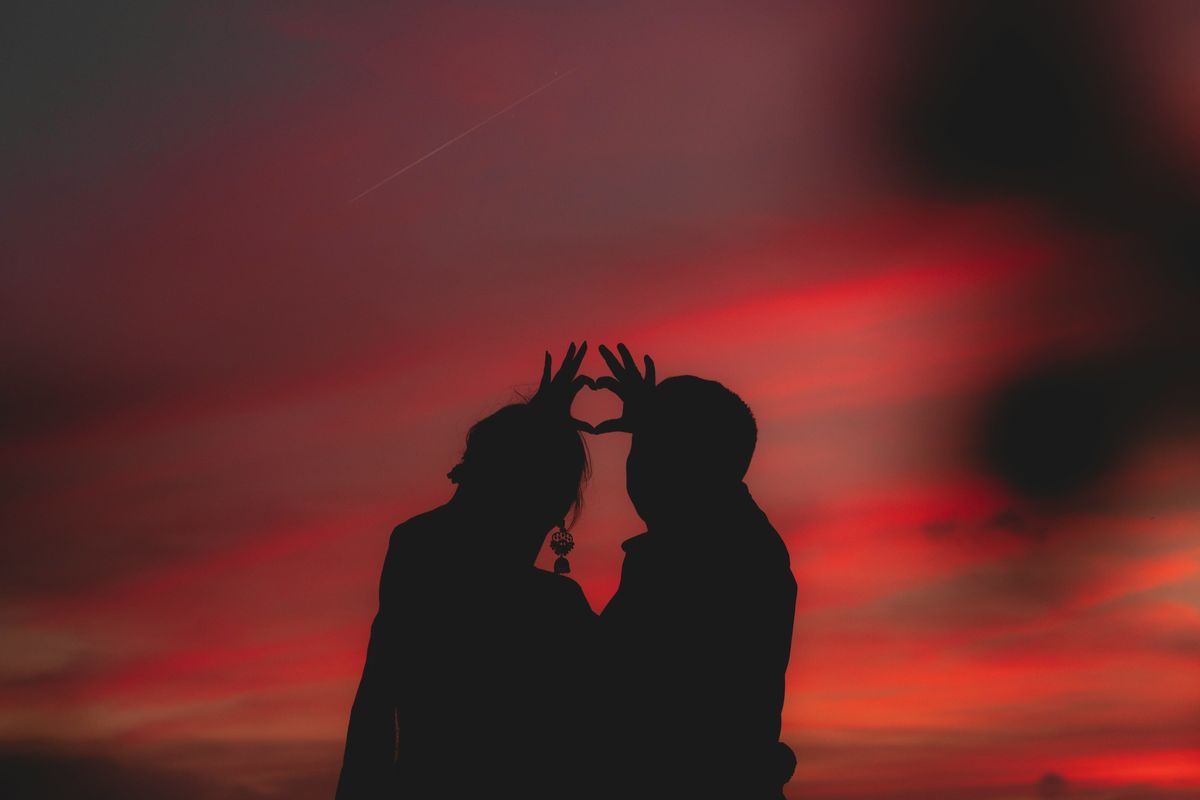 Silhouetted couple forms heart with sunset sky.