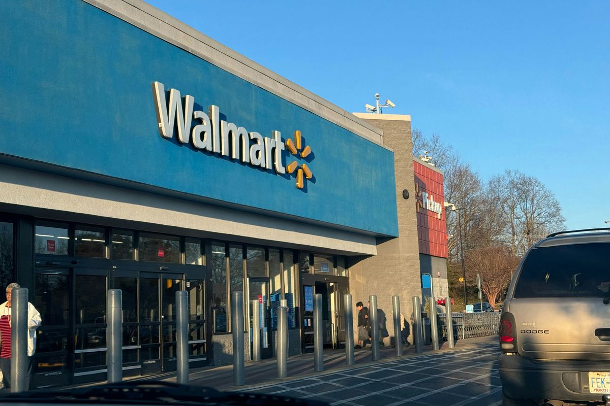 Walmart store entrance with a blue sign and parked cars in daylight.