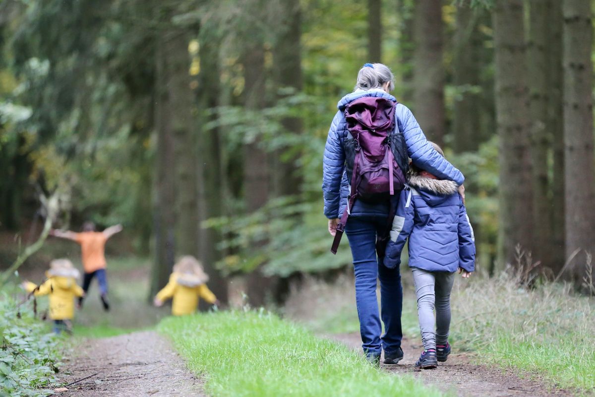 Woman and child walking on a forest path, children playing ahead.