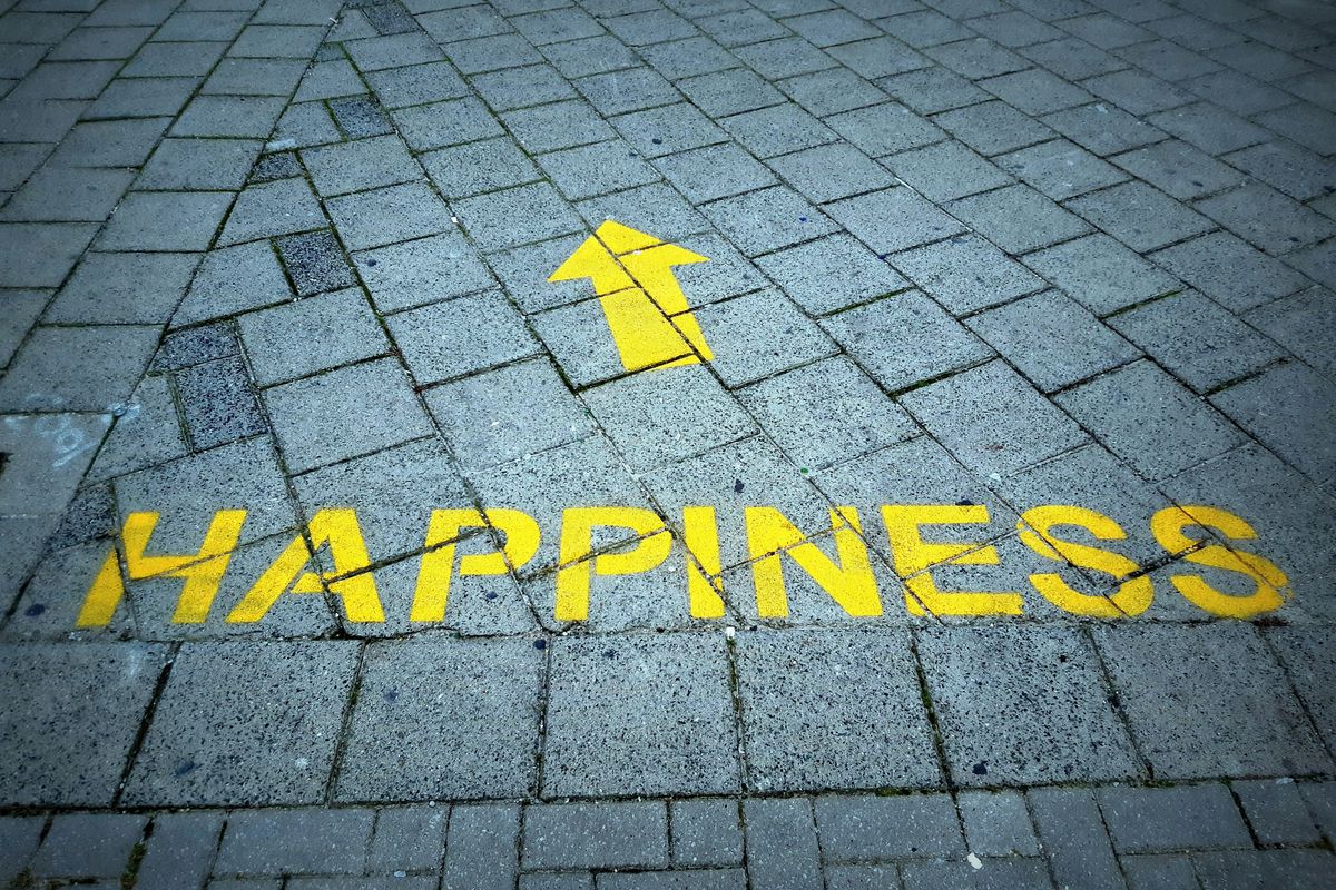Yellow "Happiness" and arrow painted on gray brick pavement.