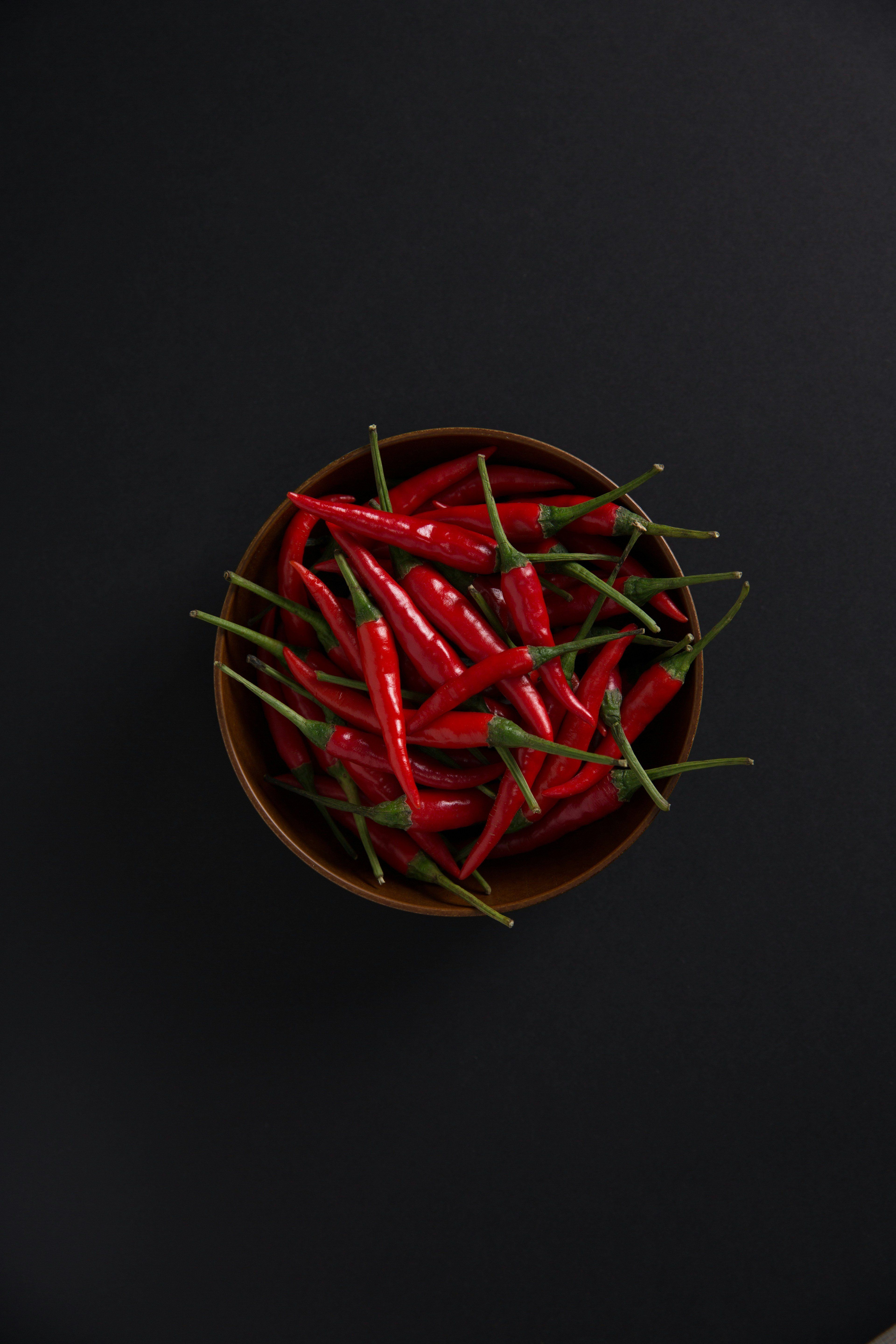 A bowl of fresh red chili peppers on a black background.