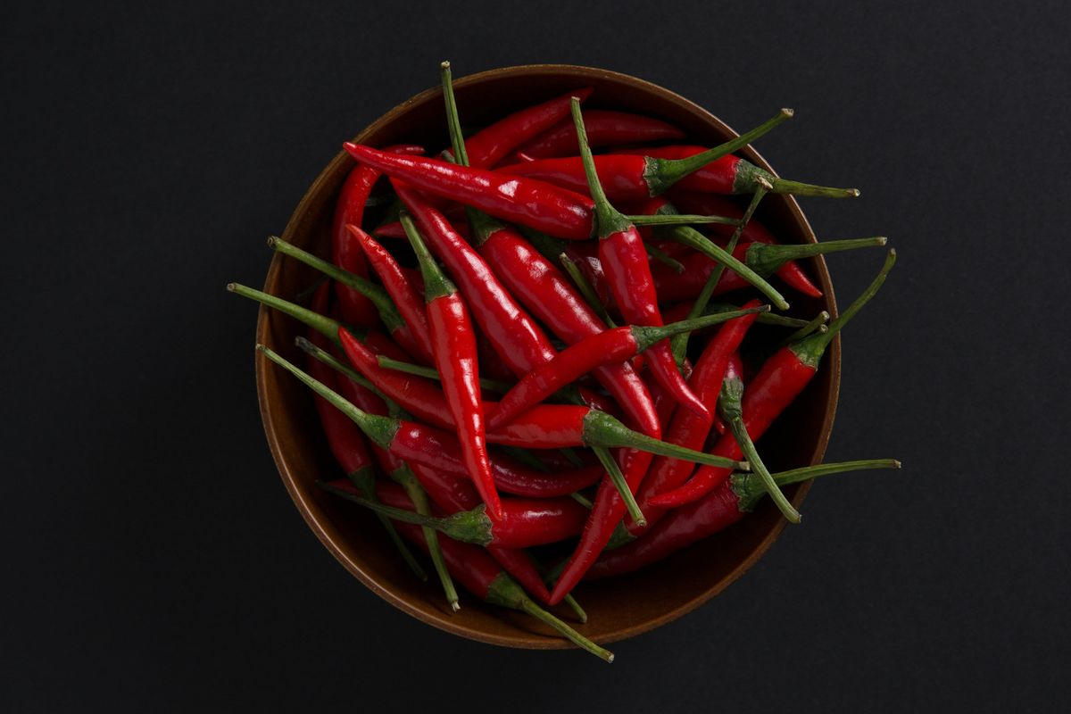 A bowl of fresh red chili peppers on a black background.