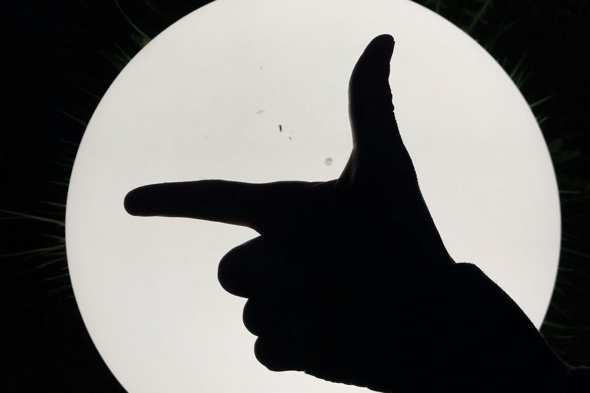 Silhouette of hand pointing like a gun against a bright, circular light source at night.