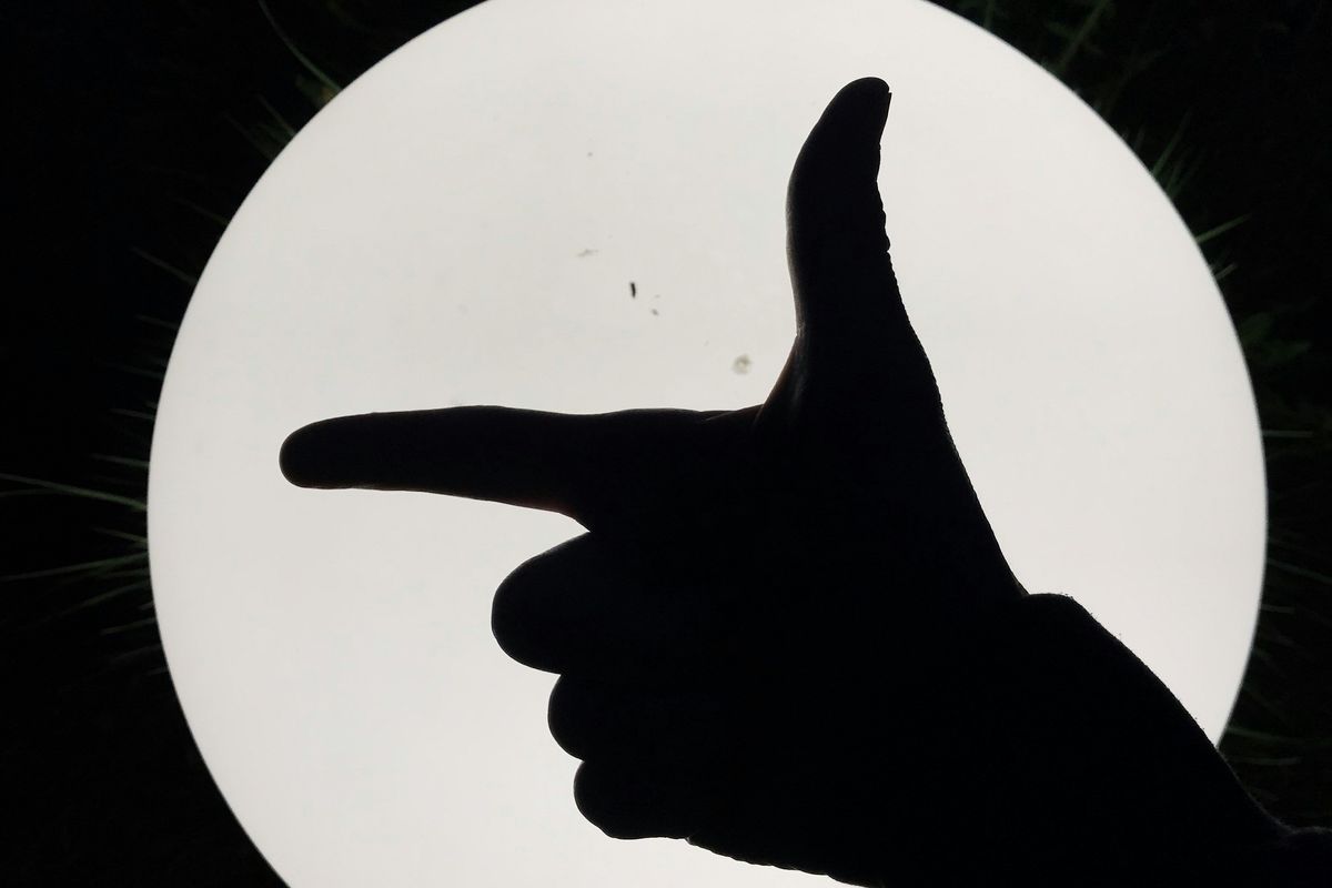 Silhouette of hand pointing like a gun against a bright, circular light source at night.