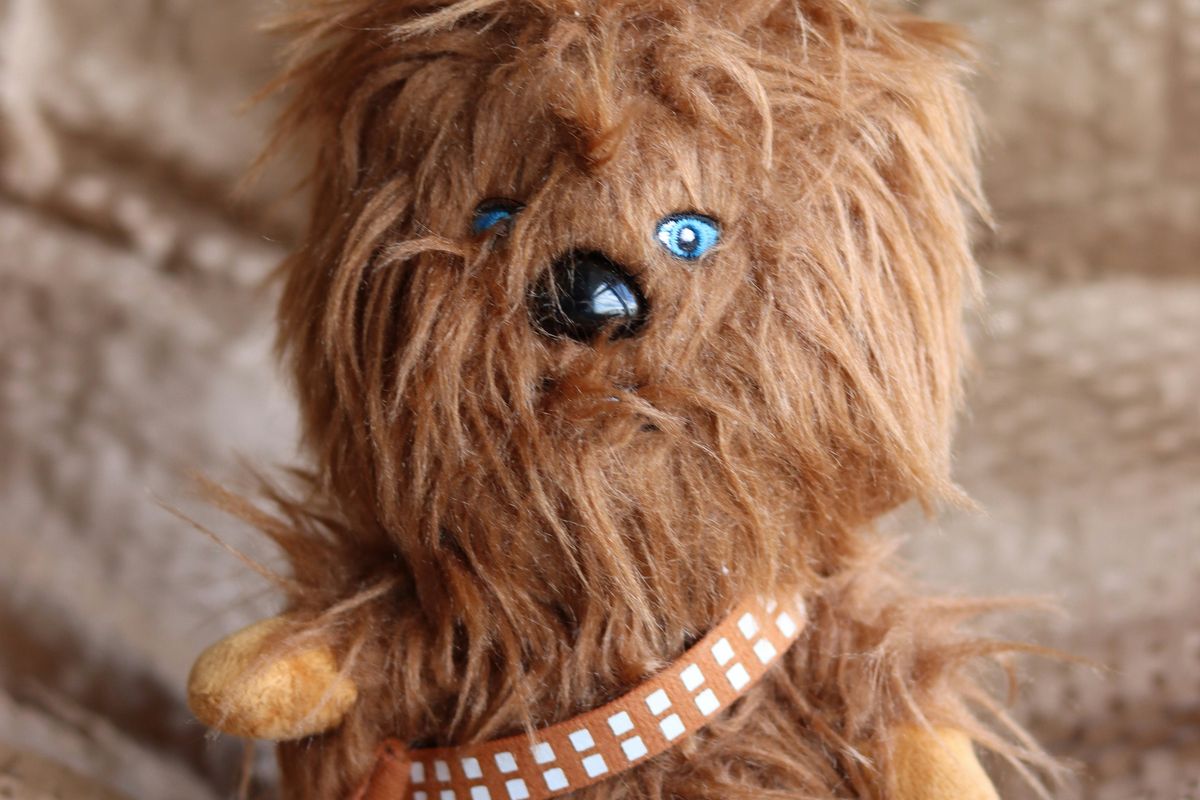 Fluffy brown stuffed toy with blue eyes, sitting on a textured beige surface.