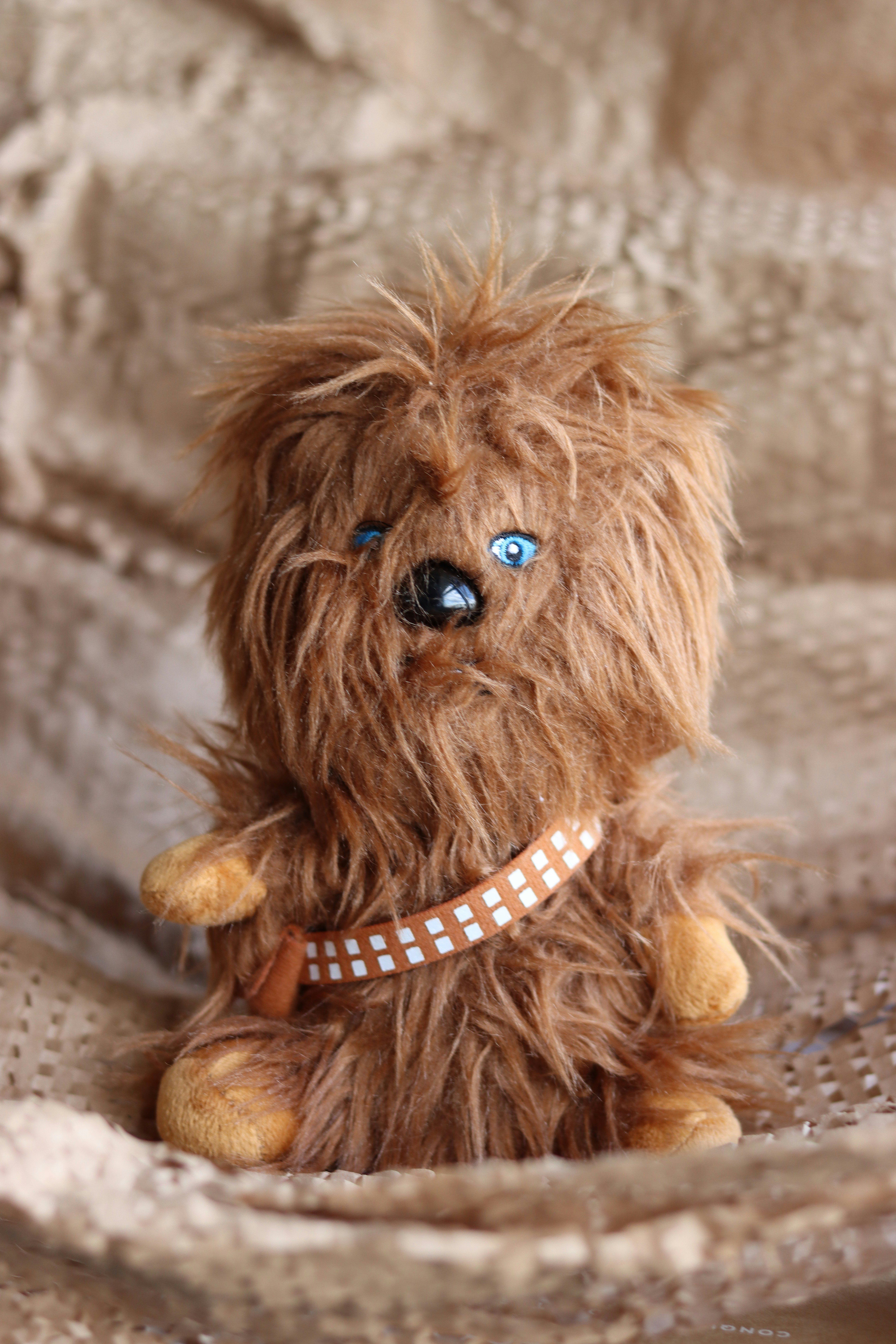 Fluffy brown stuffed toy with blue eyes, sitting on a textured beige surface.