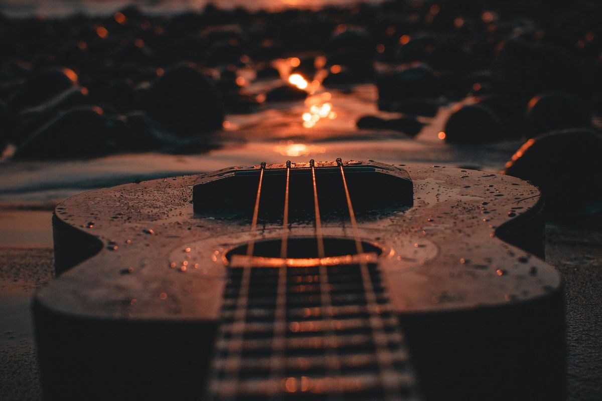 Guitar on a pebble beach at sunset, reflecting the warm glow of the sun.