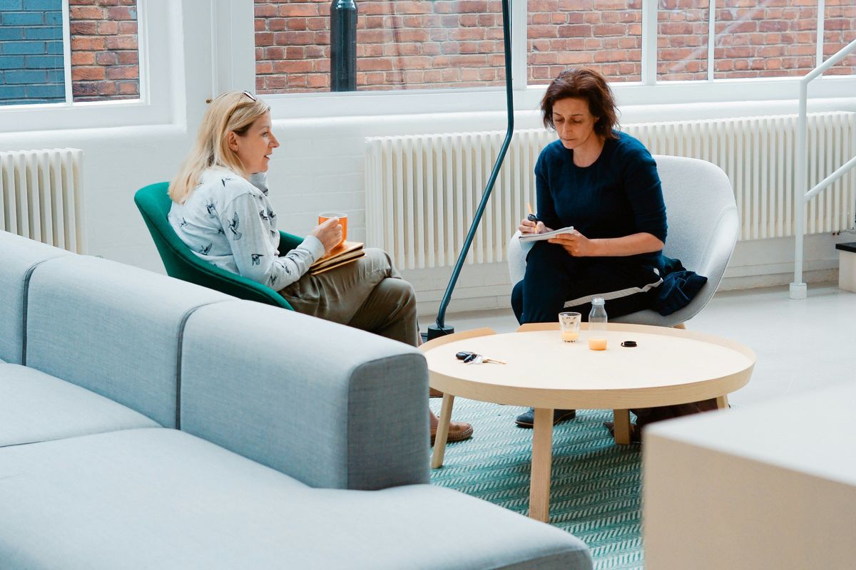 Two people sit and chat in a modern, light-filled office lounge.