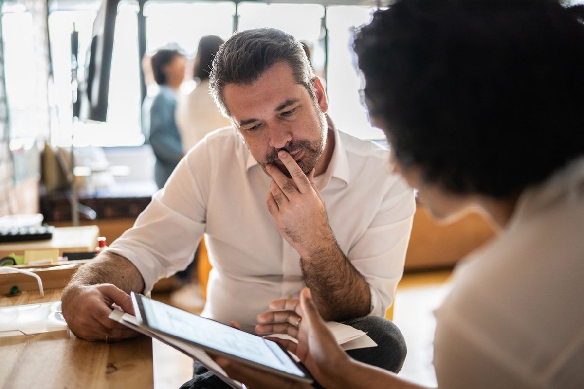 Mature man looking at a digital tablet that a colleague is showing at work stock photo
