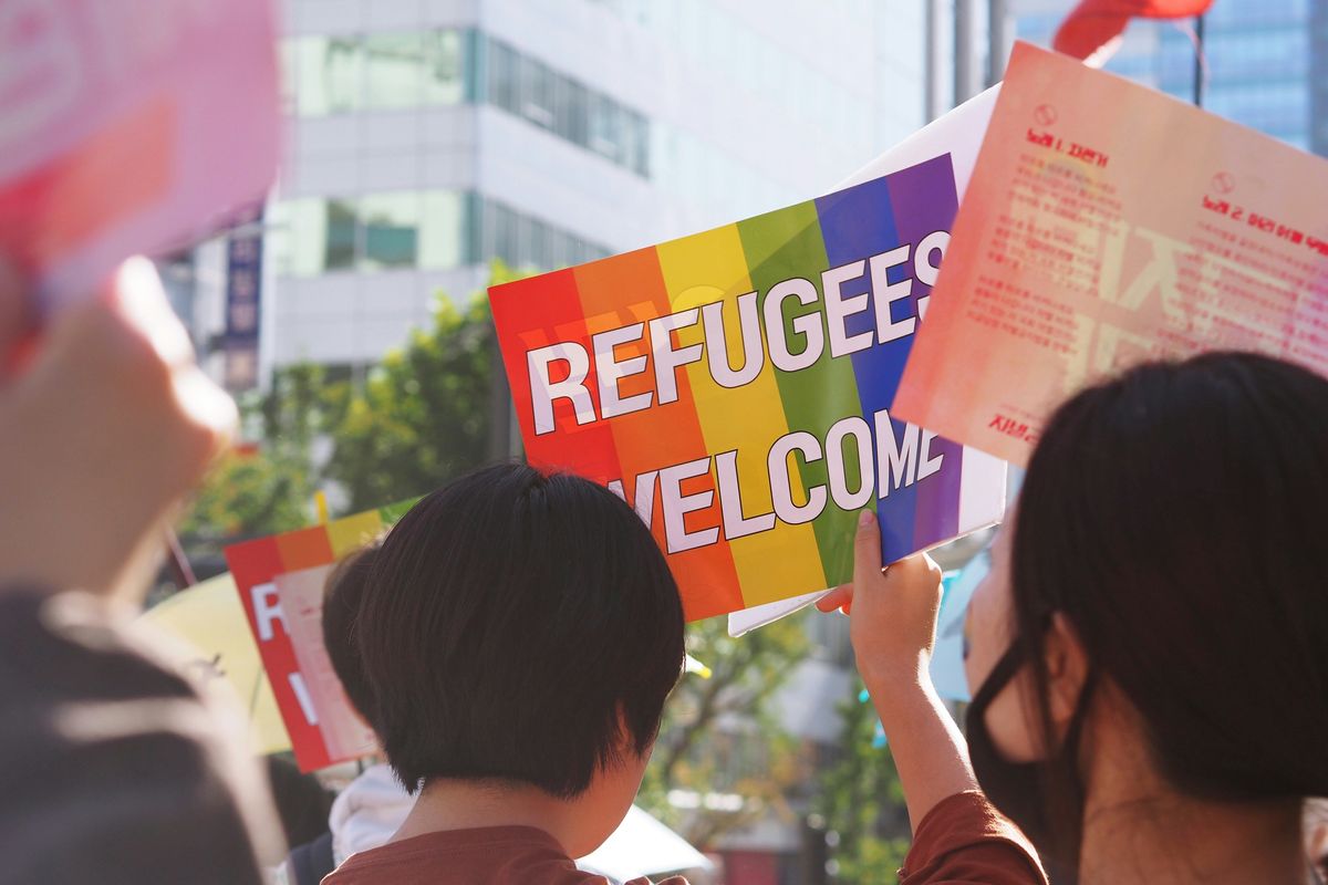 People holding a sign reading "Refugees Welcome" with rainbow colors at a gathering.