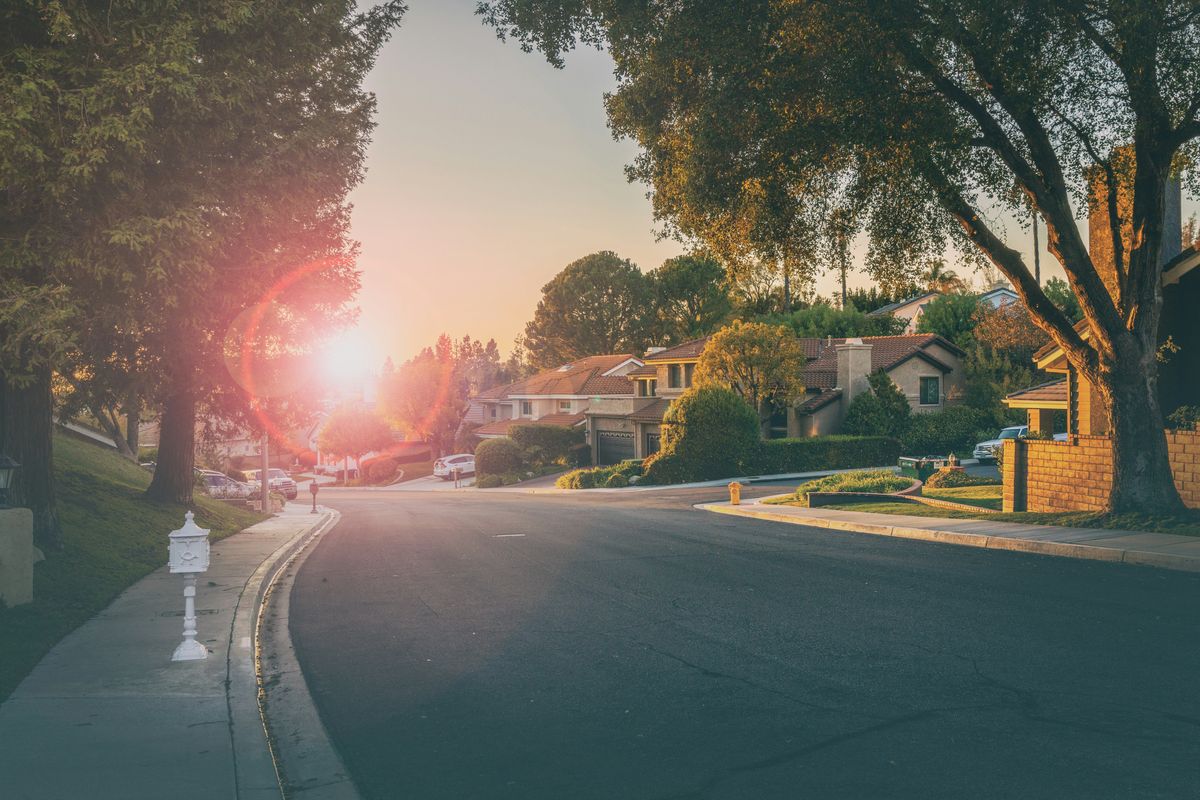 Sunset over a quiet suburban street lined with trees and houses.