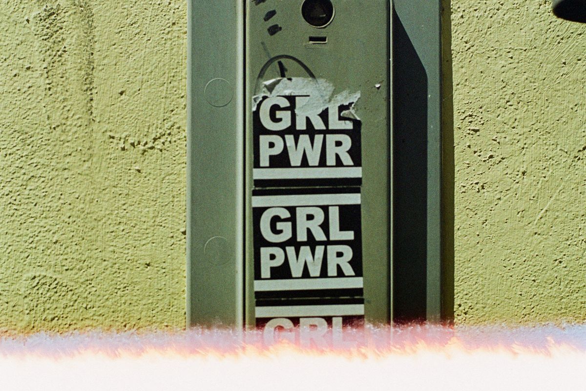 Intercom on wall with "GRL PWR" stickers and a light leak at the bottom.