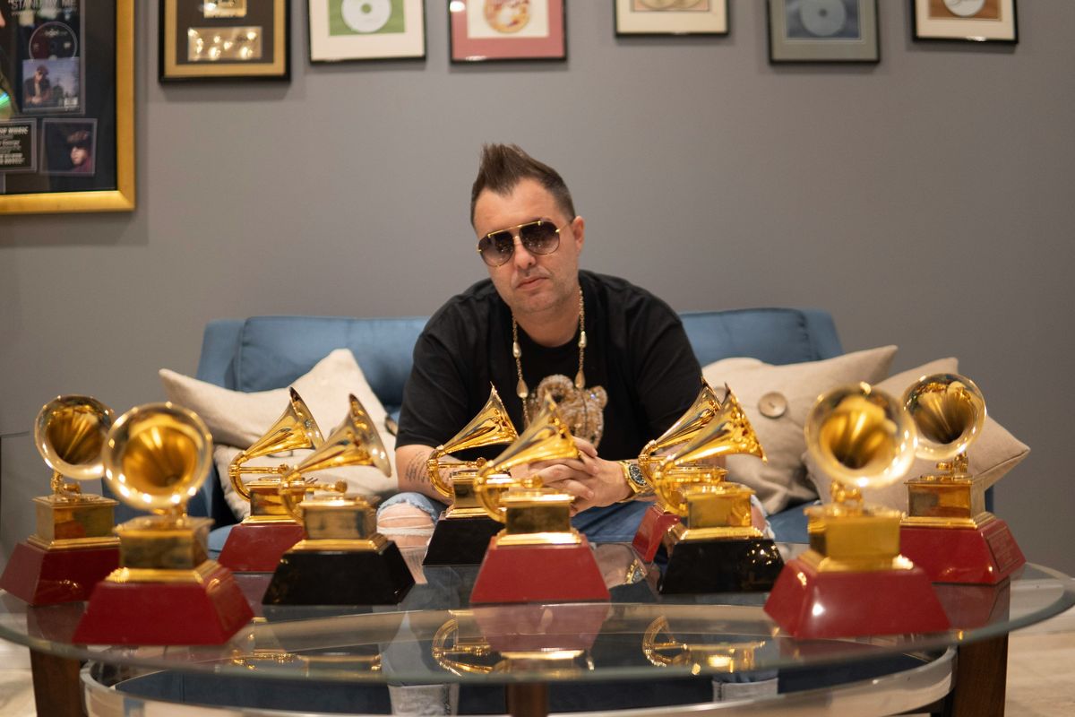 Person with multiple Grammy awards on a glass table in a room with framed records.