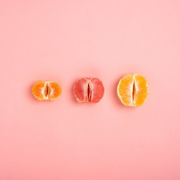 tangerine, grapefruit and orange cut in half on a peach background as a symbol of the vagina and female fertility, no people