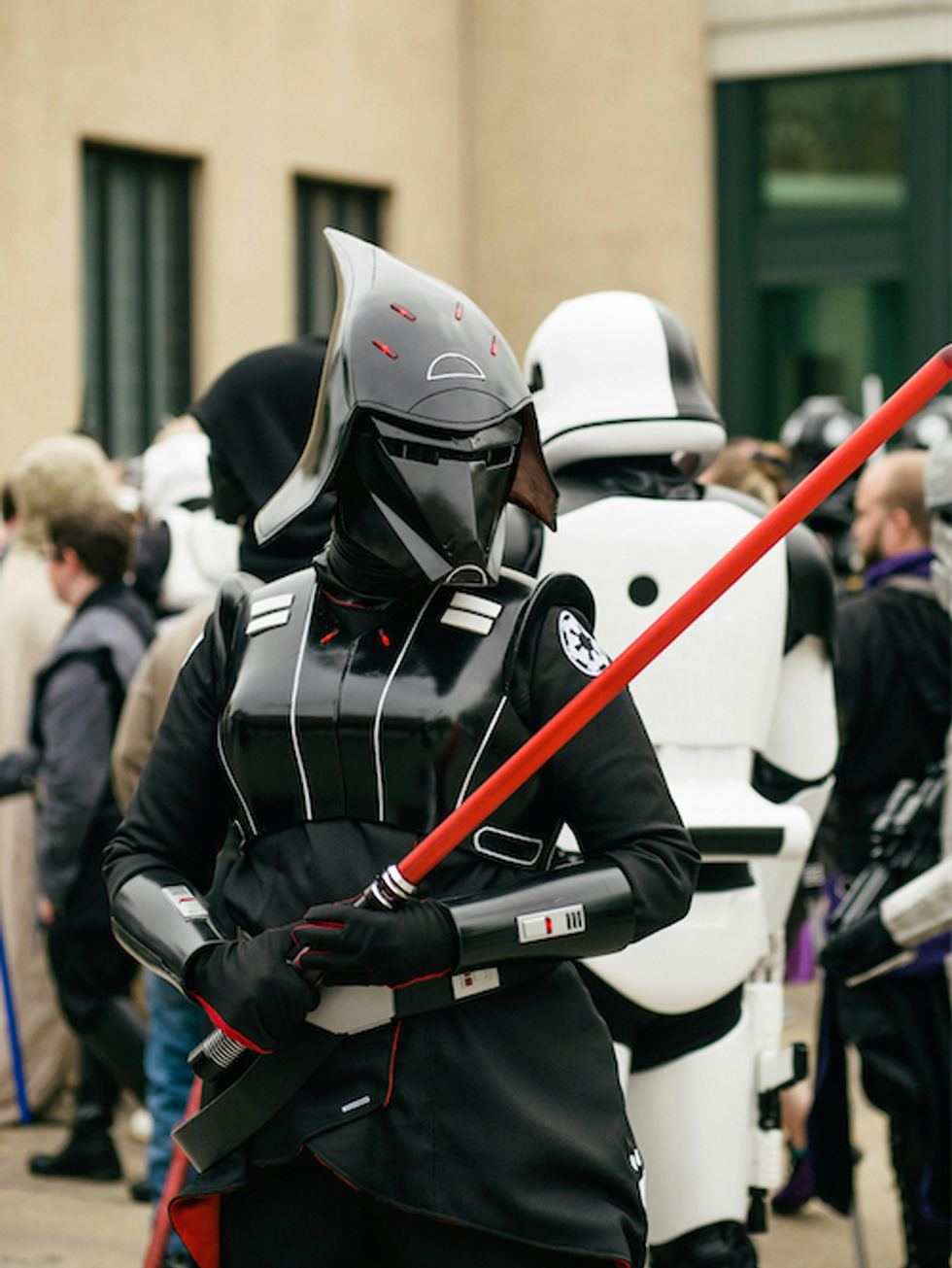 Person in Black Long Sleeve Costume and Black Helmet Holding Red Stick