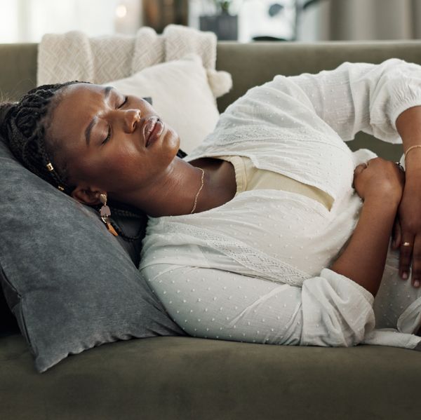 Home, pain and black woman on a couch, cramps and stomach with sickness, suffering and disease in the living room. African person, apartment and girl with abdominal problem, tummy ache and period