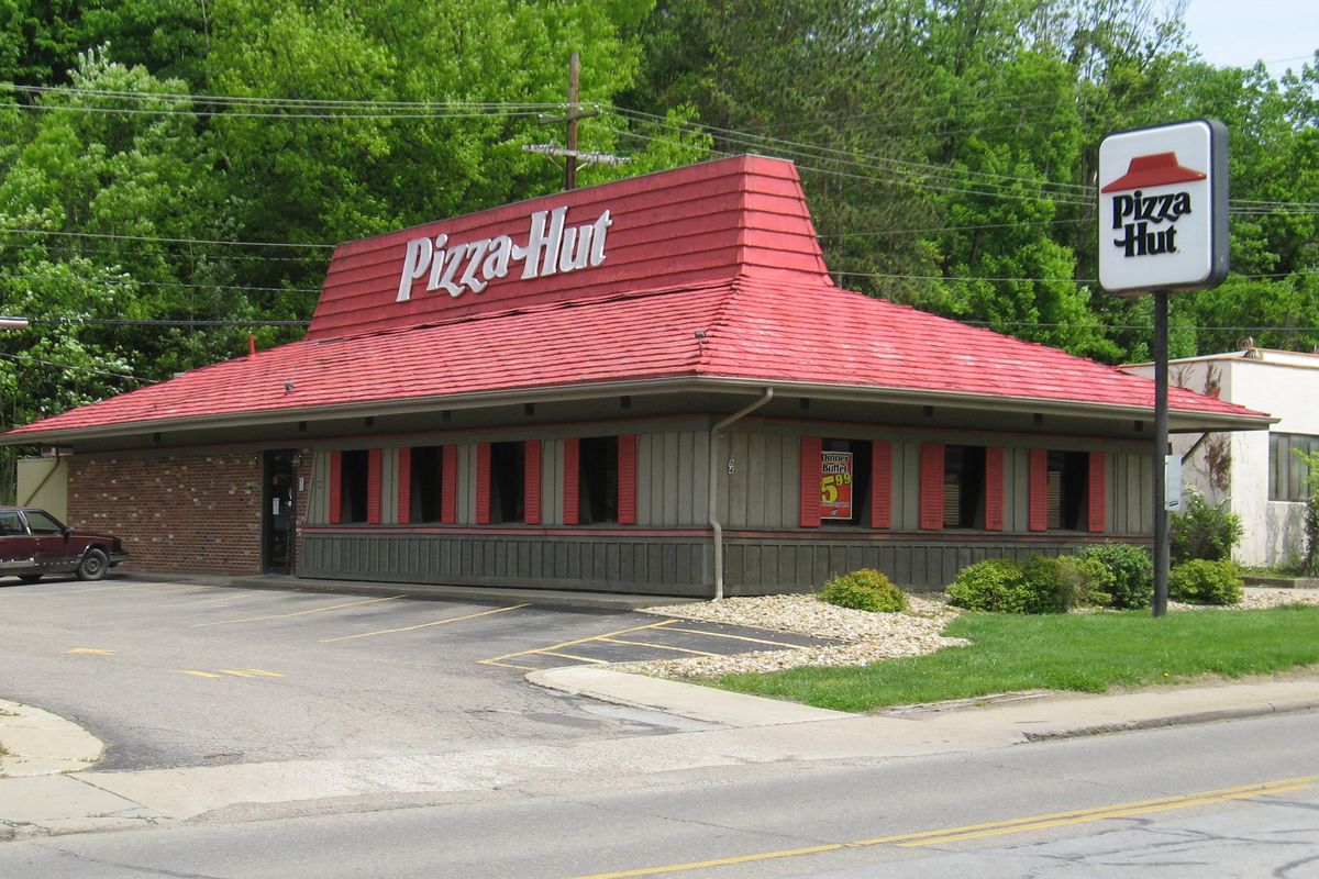 A classic Pizza Hut restaurant with a red roof and surrounding greenery.