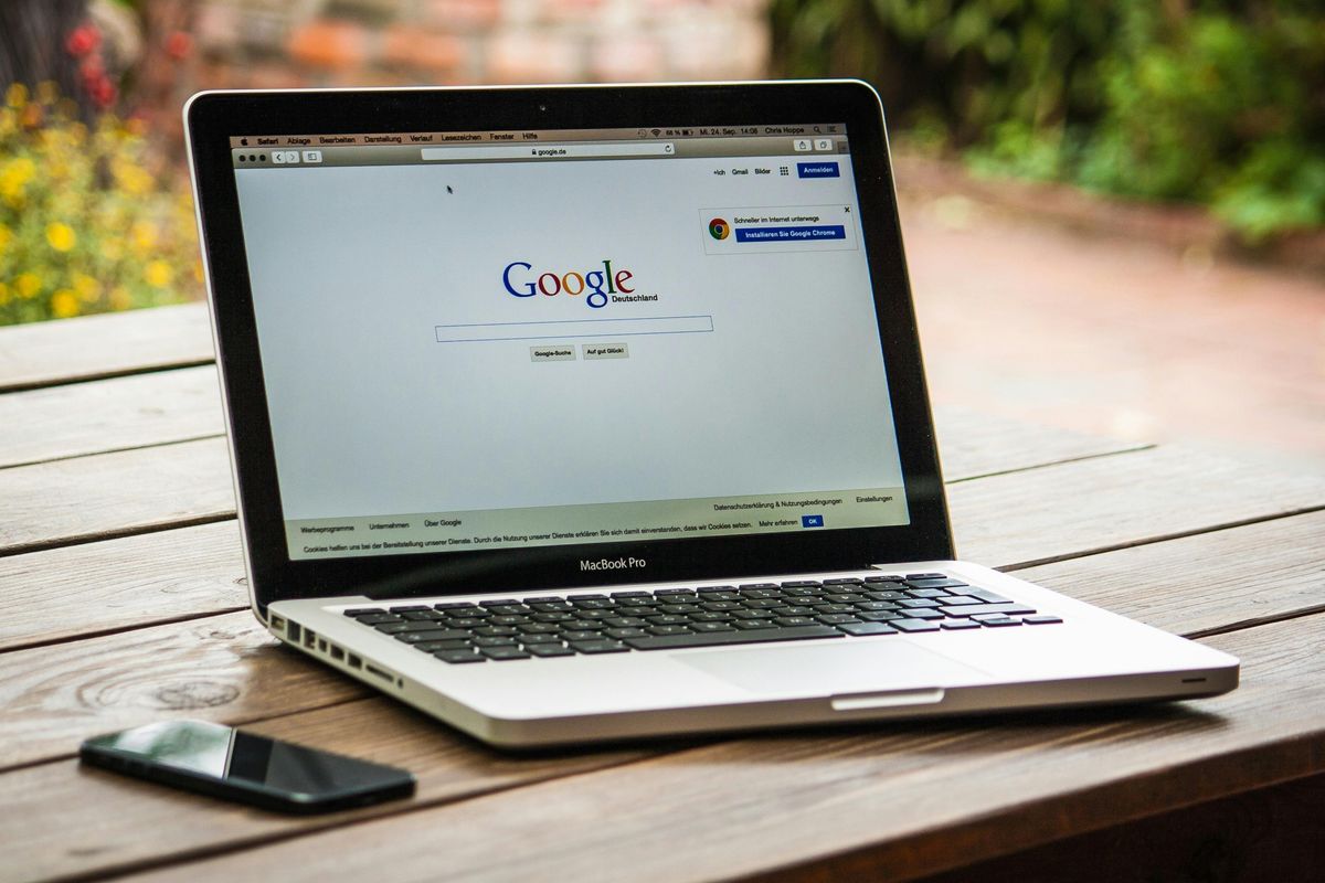 photo of a MacBook Pro on a picnic table with smartphone and google search home page on the screen