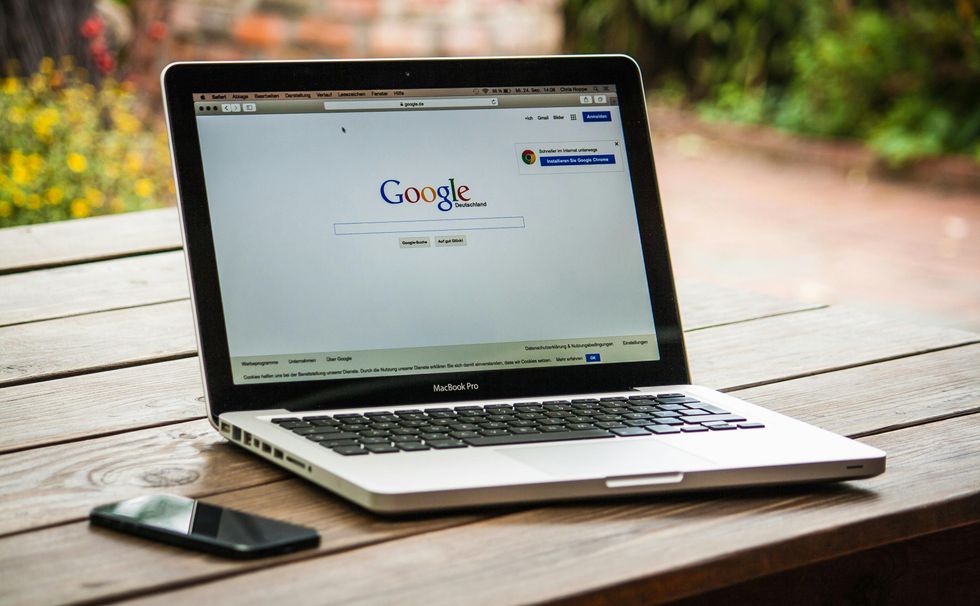 photo of a MacBook Pro on a picnic table with smartphone and google search home page on the screen