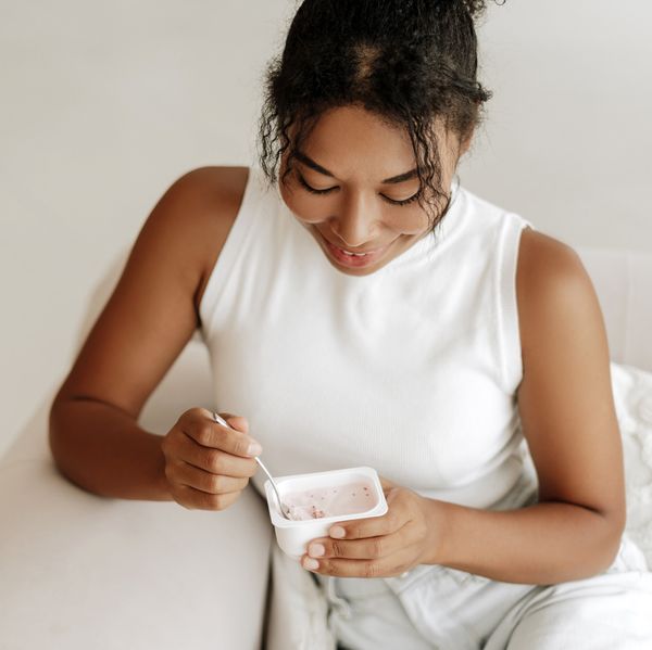 Young woman smiling while eating yogurt at home, symbolizing probiotics and vaginal health for preventing yeast infections after sex.
