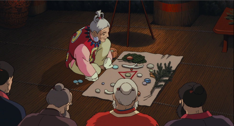 A scene from early in the Japanese animated film "Princess Mononoke" (1997). The village elder tells the fate of the cursed Prince using objects laid about the hut.