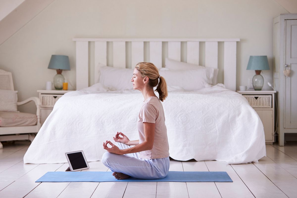 A woman meditating in a bedroom on a yoga mat