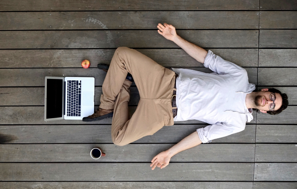 A man leaning back on a porch, hands out, eyes closed with a computer in front of him