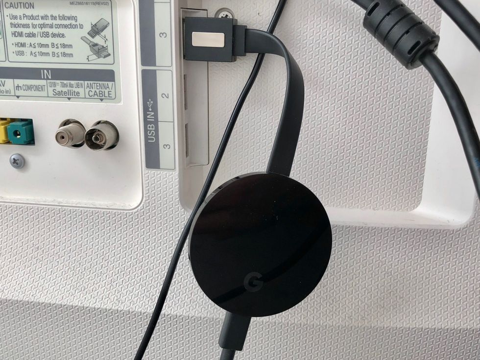 Google Chromecast connected to the back of a TV via HDMI slot.