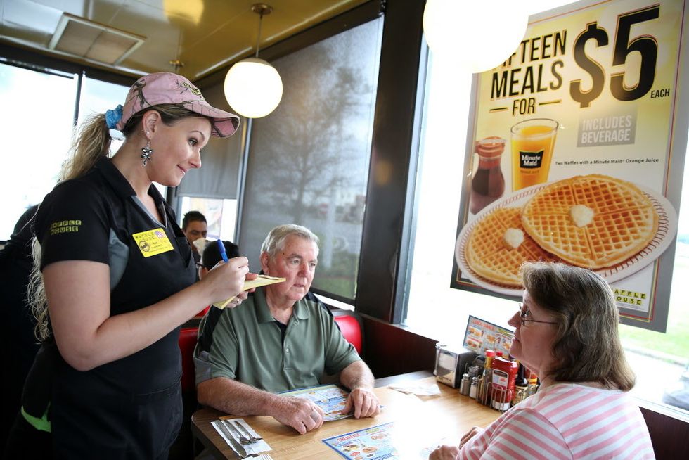 A woman in a pink camo hat serves a couple at Waffle House.