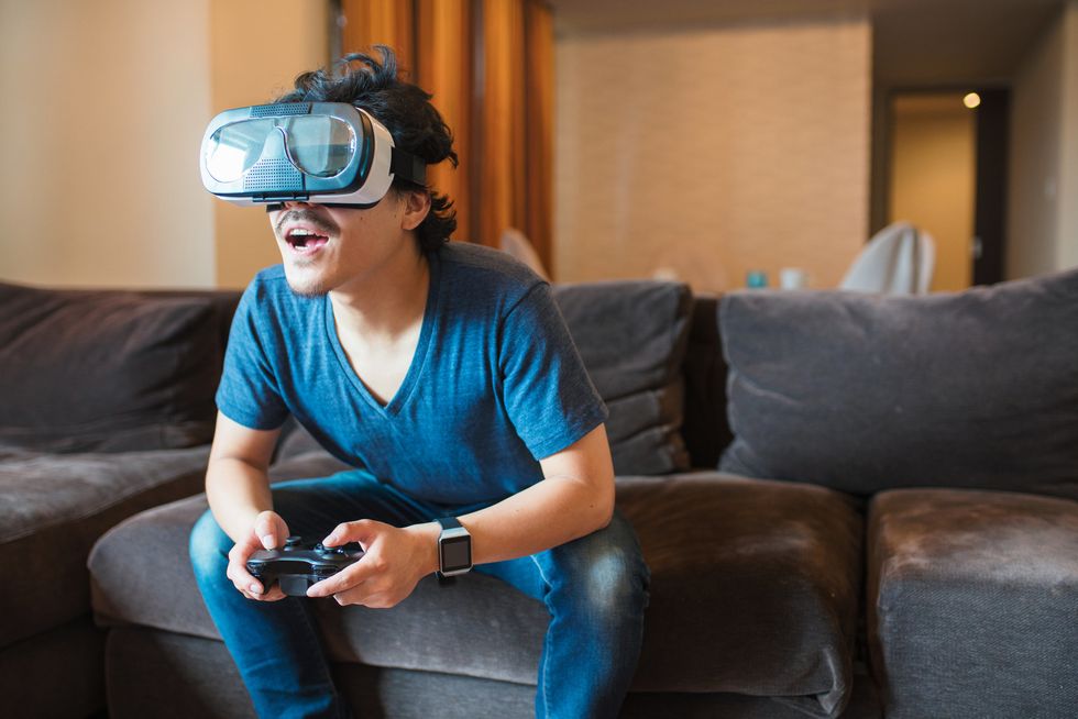 A man on a couch wearing a VR Headset playing video games.