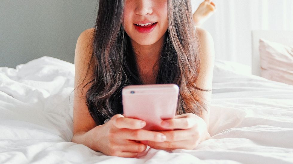 sexy asian woman sexting on smart phone in bed