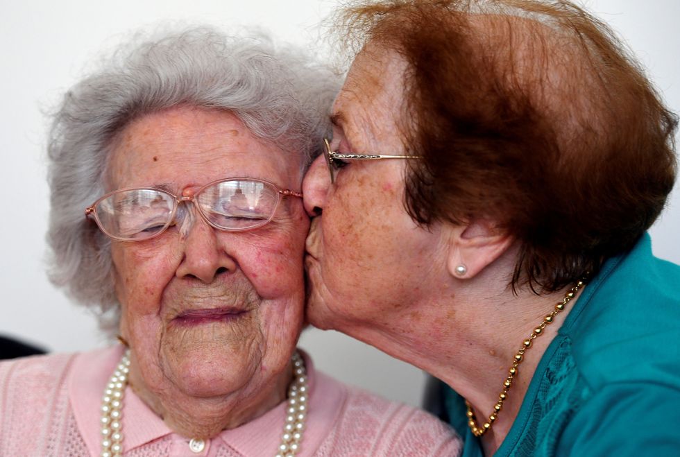 A senior being kissed by another old woman.