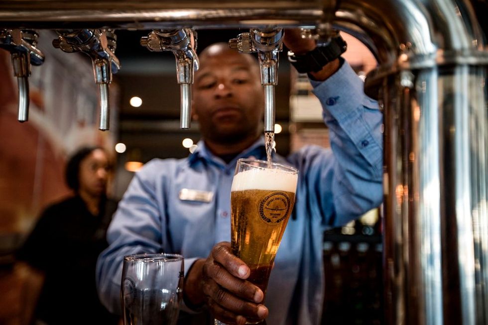 Barman Oscar Cetane (L) pours a pint at the Airport Craft Brewers, Africa's first airport brewery, at OR Tambo International Airport in Johannesburg on October 17, 2017. (Photo by Gulshan Khan/AFP/Getty Images)