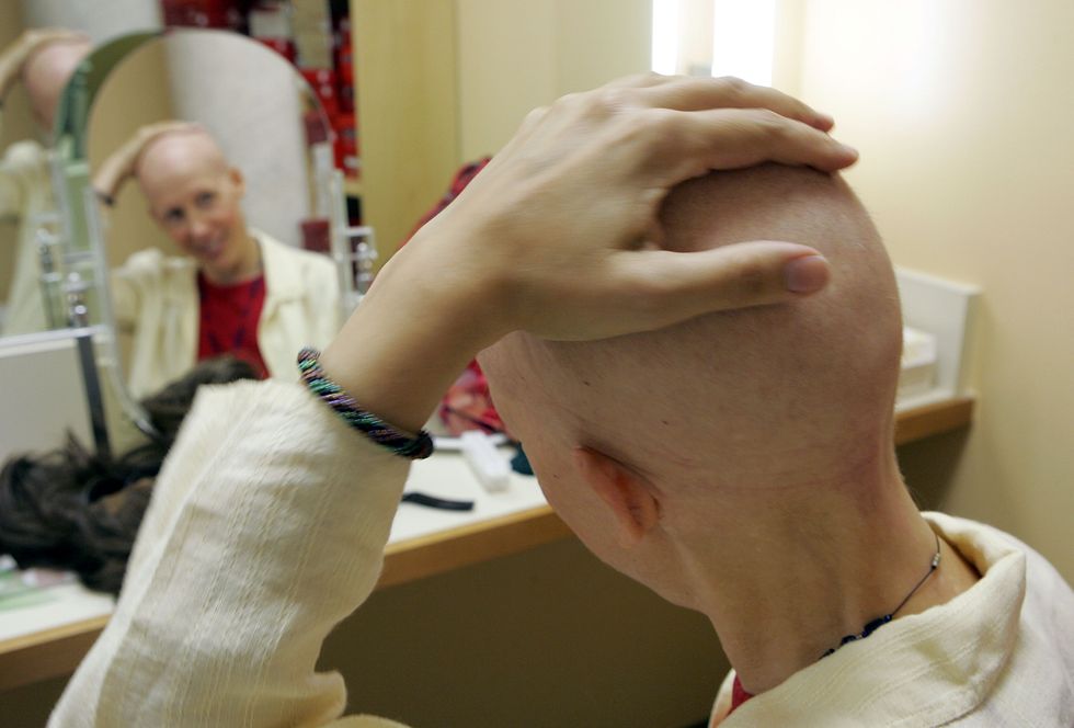 Woman with cancer looks at her head in the mirror.