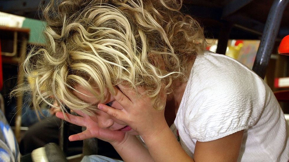 A kindergarten student hides under her desk during a classroom lockdown drill February 18, 2003 in Oahu, Hawaii. (Photo by Phil Mislinski/Getty Images)