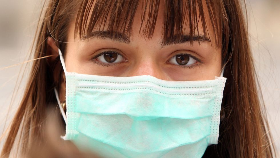 A woman wearing a surgical mask to prevent the transmission of airborne infection walks in Westminster on July 30, 2009 in London, England. (Photo by Oli Scarff/Getty Images)