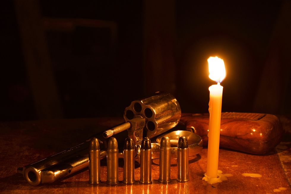 Candle burning next to a revolver and six bullets.