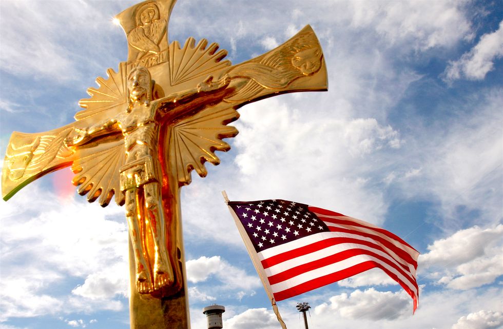 A golden statue of Jesus on the Cross next to an American flag in the breeze.