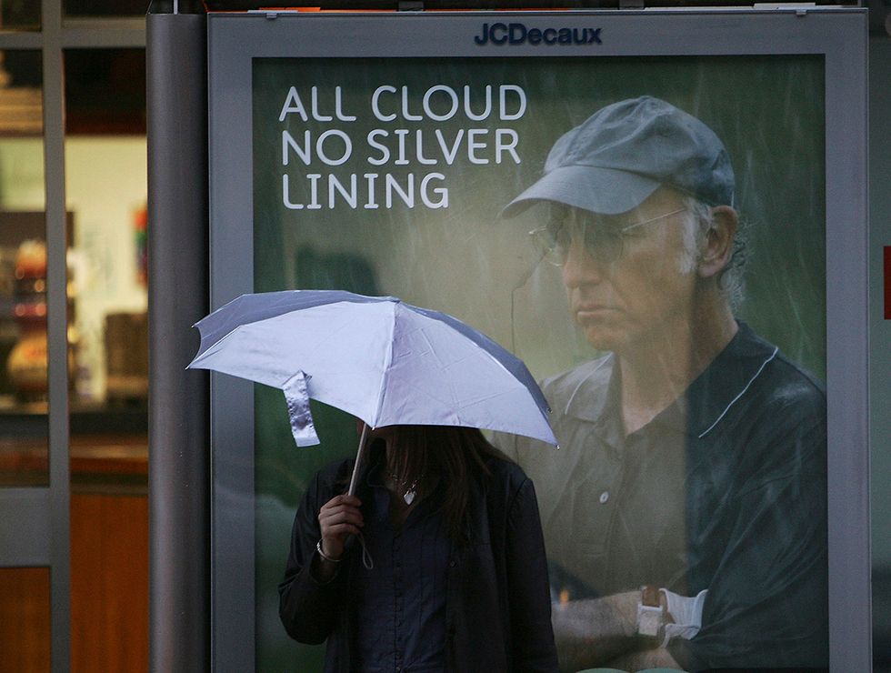 GLASGOW, UNITED KINGDOM - OCTOBER 10: A woman waits for bus on her way home from work in Scotland. Behind her, a poster of Larry David with the words "All cloud, no silver lining."