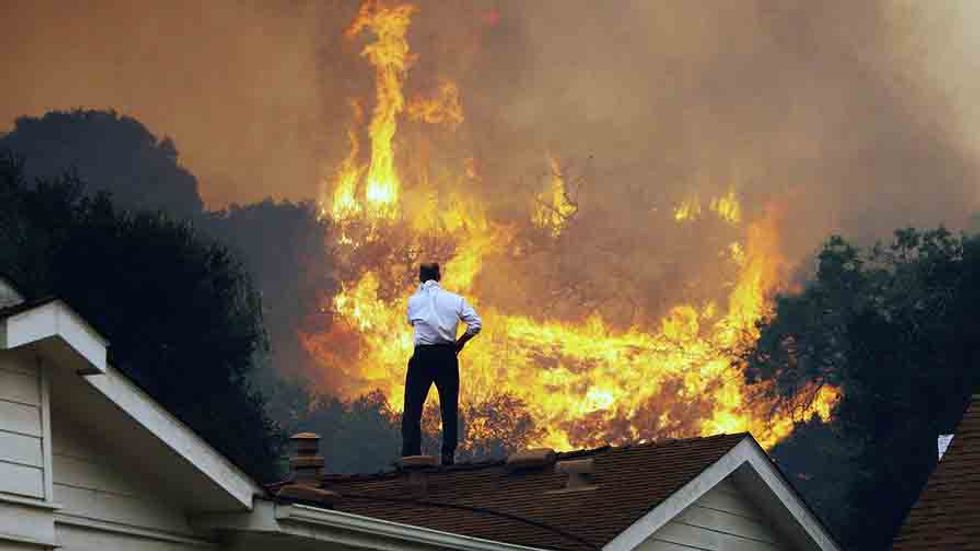 A man on a rooftop looks at approaching flames as the Springs fire continues to grow on May 3, 2013 near Camarillo, California. (Photo by David McNew/Getty Images)