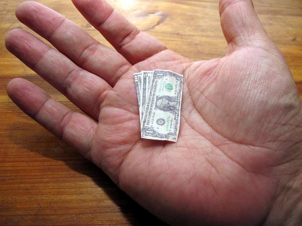 Some miniature dollar bills laid out in someone's palm. Shrinking money.