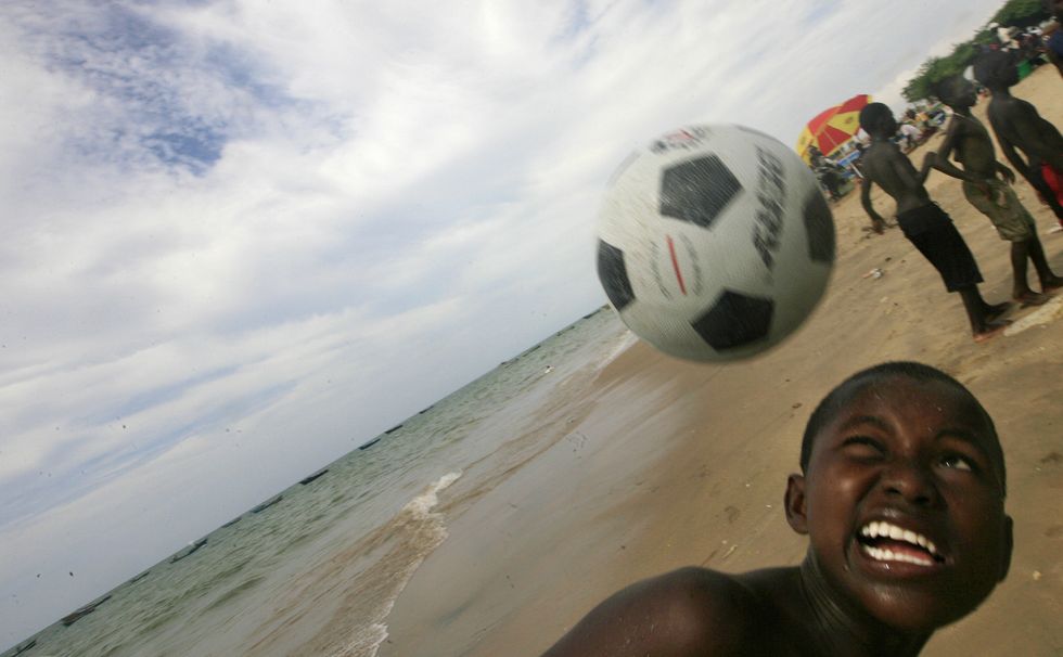A young boy on the beach, about to head a soccer ball.
