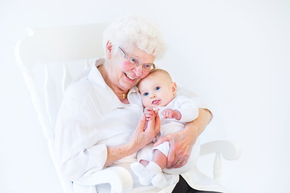 A white-haired woman in a hospital bed with a new-born baby.