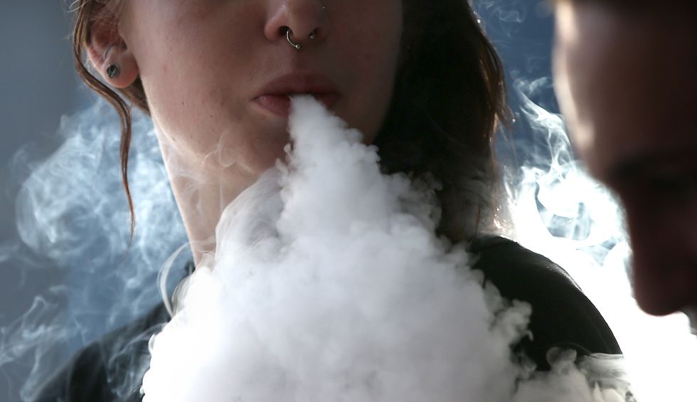 A young woman exhaling a thick cloud of e-cigarette smoke.