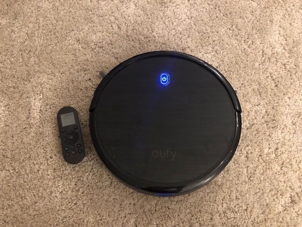 A photo of the Eufy RoboVac BoostIQ 11S, a round circle-shaped robot in black on a beige rug, with a small blue light on its top